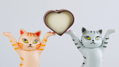 Cropped photo of toy kittens carrying a heart-shaped candy made of black and white chocolate. Pale blue background.
